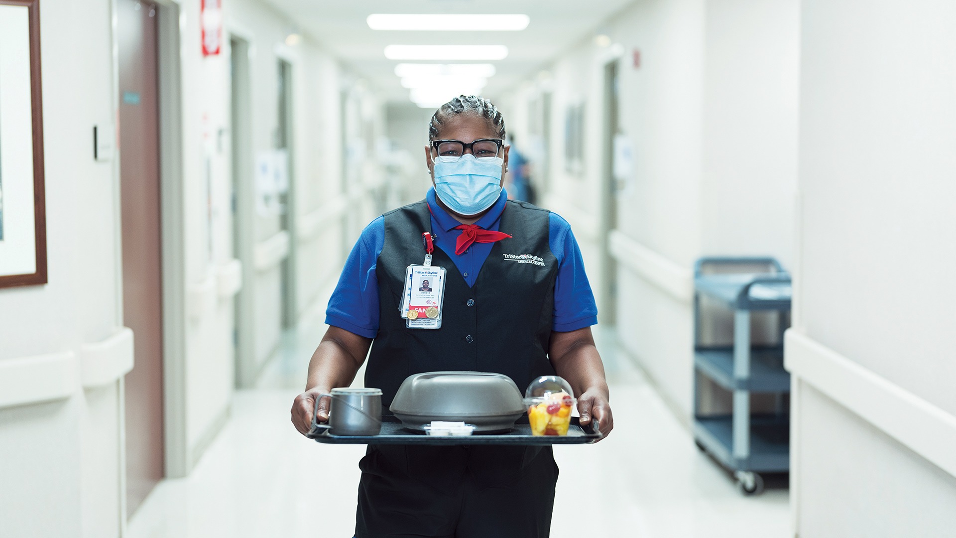 Hospital food service worker carrying a meal tray down a hallway