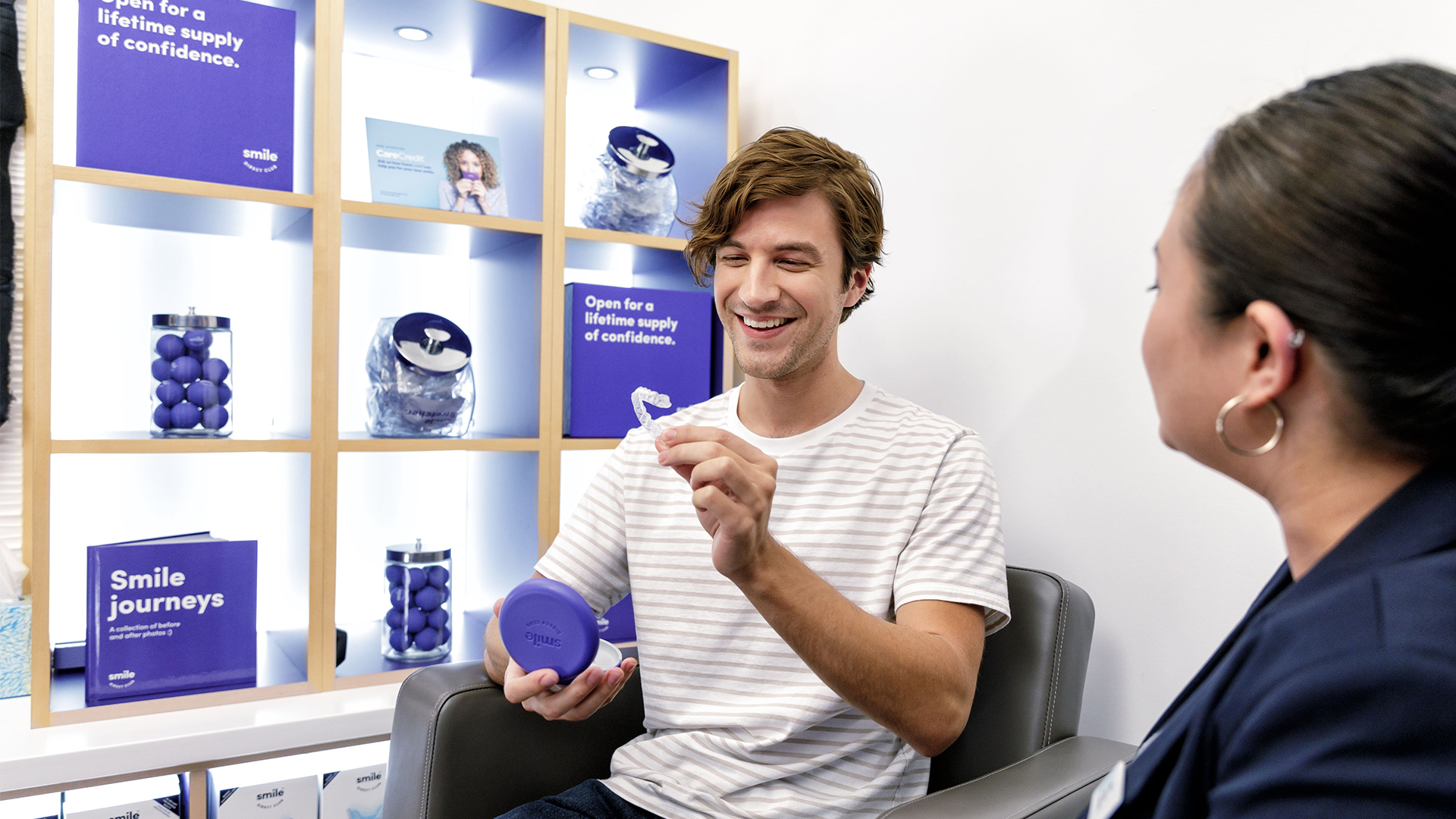 A smiling man showing his SmileDirectClub clear aligner to a store associate inside a SmileDirectClub retail location